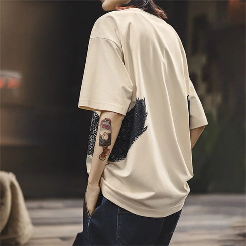 Person wearing a beige oversized t-shirt with a tattoo on the arm, standing outdoors.
